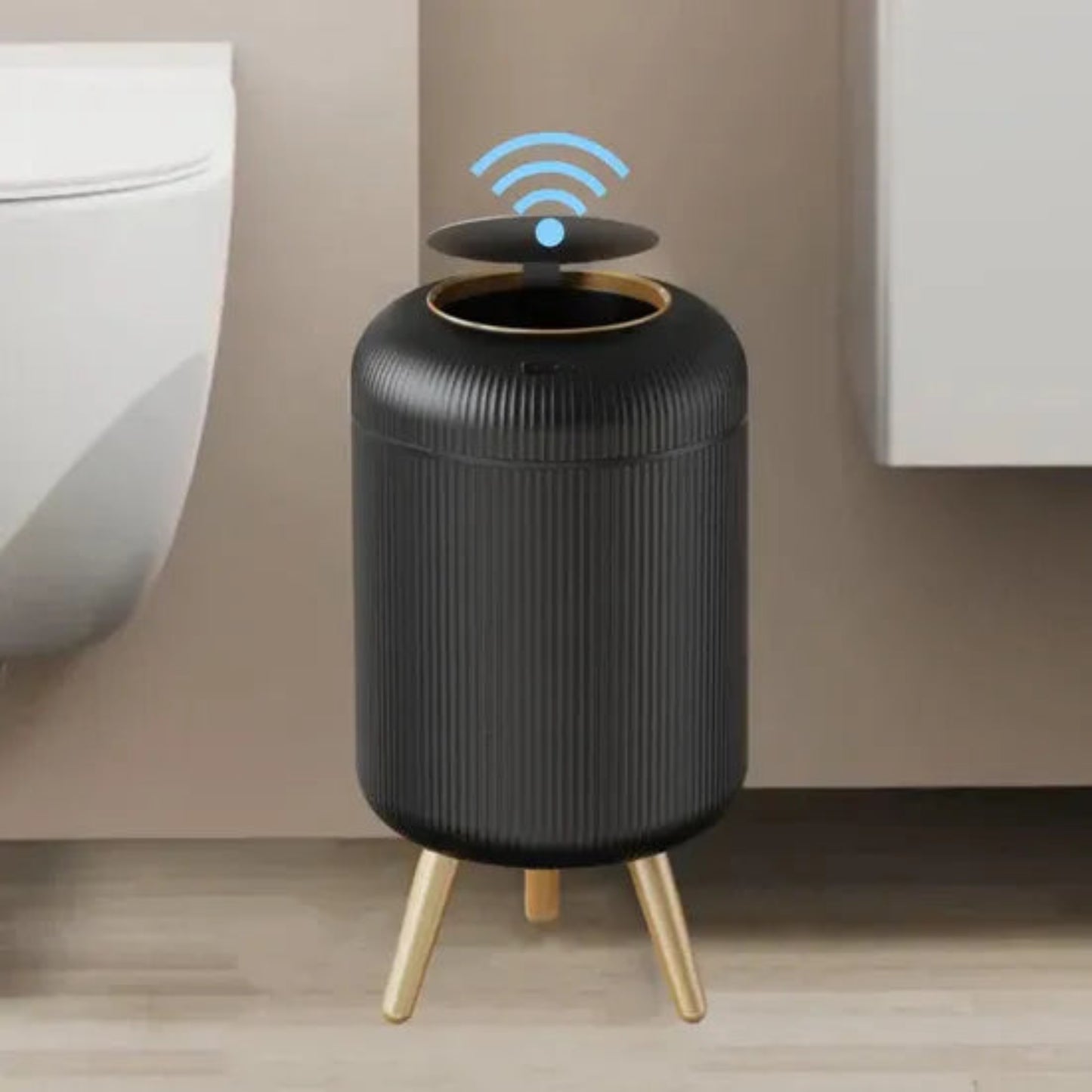 Black cylindrical device with gold legs on a wooden floor against a beige wall.
